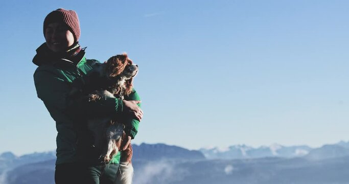 Woman hiking with dog in Alps Mountains. Young female solo tourist holding cavalier king charles spaniel companion breed dog, playing and cuddling her pet on winter trail, Autria and Germany travel