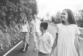 Cheerful, happy family, father, mother, son and daughter enjoying walk play outdoor. Lifestyle concept. Family in white clothes on walkway. Green forest background. Black and white.