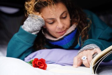 Young woman lying reading a book in her camper van with a rose. Sant Jordi Day in Catalonia