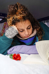 Young woman lying reading a book in her camper van with a rose. Sant Jordi Day in Catalonia