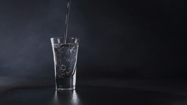 A Stream of Water pours into a Glass against a grey background. Water splash. Close up