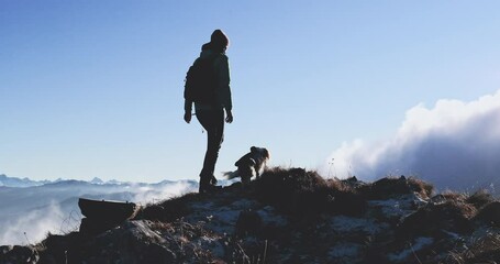 Woman hiking with dog in Alps Mountains. Young female solo tourist with backpack on winter trail with Cavalier King Charles spaniel companion breed dog having adventure with clouds view in Austria.