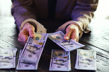 women's handcuffed hands hold dollars on a dark wooden background