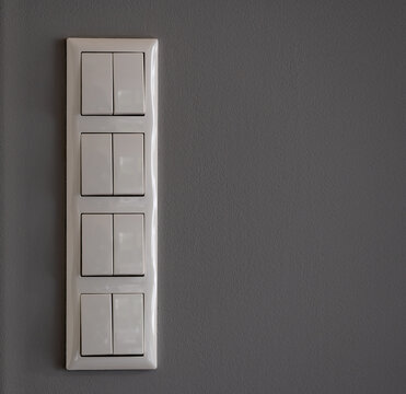 Eight white light switches on a grey wall.
