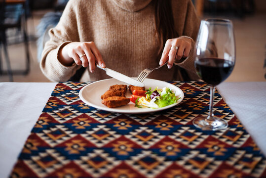 Closeup image of unknown woman eating meat and salad at table in the restaurant