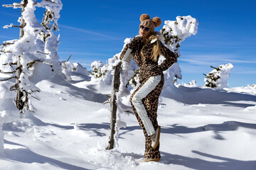 Beautiful shapely female model is wearing sexy winter ski suit and winter hat and is posing in snow...