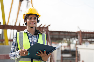 Asian woman engineer holding document smiling at construction site. Confident female Indian wearing...