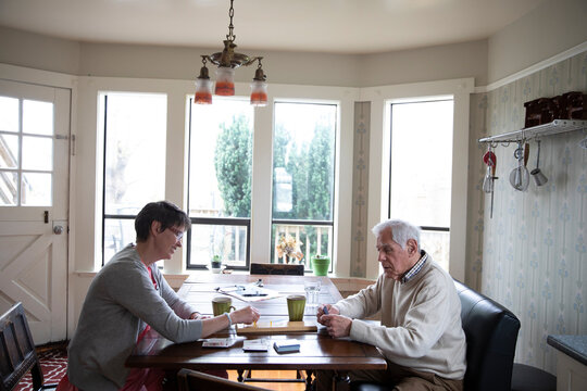 Home caregiver and senior man playing cribbage at kitchen table