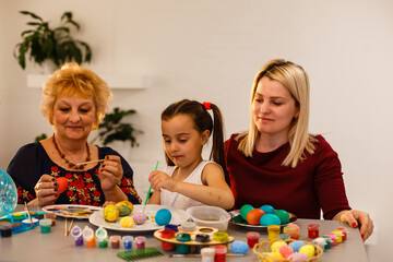 Naklejka premium Little girl and her grandmother painting Easter eggs at home.