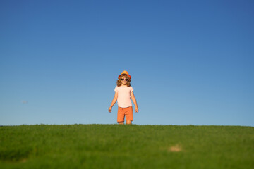 Kid boy running on green grass near blue sky in spring park. Sporty child boy runner running in summer park. Active kids, sport children.