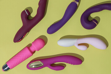 A lot of different dildo vibrators on yellow background with shadows. Sex toy for adult