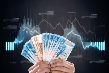 Hand holding stack of currency note with digital trading chart.