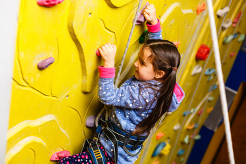 little girl climbing a rock wall indoor.