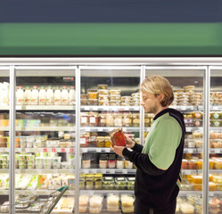 Young man shopping in supermarket, reading product information.