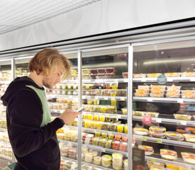 Young man shopping in supermarket, reading product information.