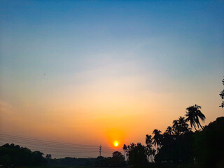 Sunset in the countryside of Bangladesh, with silhouette of palm trees.
