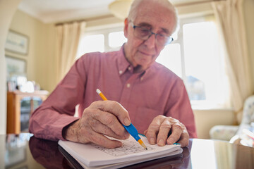 Senior Man With Arthritis Using Grip Aid On Pencil To Write In Sudoku Puzzle Book