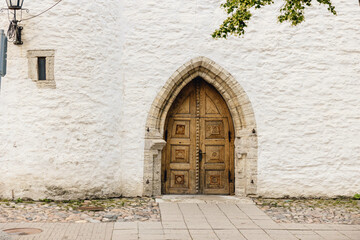 Fototapeta na wymiar Ancient wooden arched doorway set into old white wall in medieval centre of European city