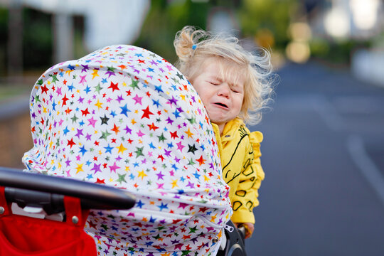 Portrait of little sad toddler girl sitting in stroller and going for a walk. Crying baby child does not want sitting in pram. Healthy daughter. Hysteric crisis of two years phase