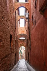 Fotobehang Narrow old street with several upstairs passages, in Siena, Tuscany, Italy © FredP