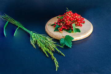 Red currants in a glass. On a wooden background, a light green napkin with leaves and red berries, on a napkin a glass transparent glass with red currant berries.