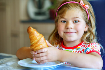 Smiling child at breakfast. Food and happy kids. The girl is eating a croissant. Cute preschool...