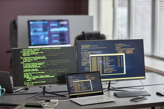 Background image of multiple computer screens with code lines at workplace desk in IT office