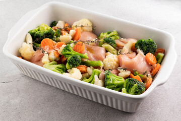 Raw vegetables and Raw chicken breasts with spices for baking in a ceramic bowl. The concept of proper nutrition.