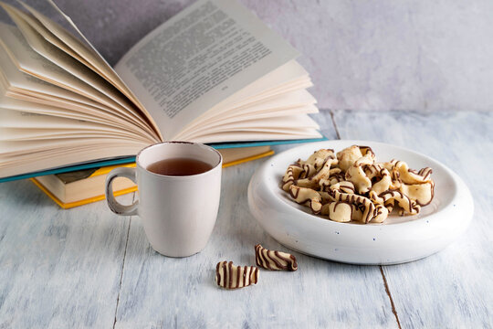 Blurred image of a cup of tea, cookies and books on a light table.