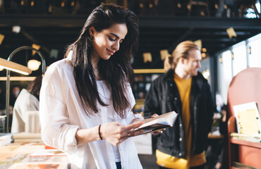 Smiling woman standing and reading book in shop