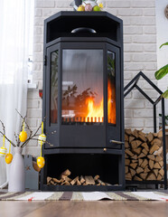 Easter decor near fireplace stove with fire and firewood. Cozy home hearth in interior with potted...
