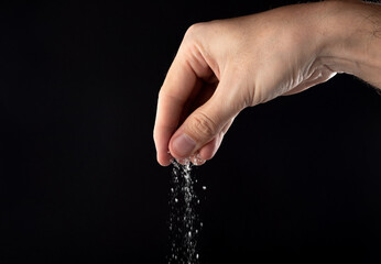 Hand sprinkling salt, salt on a black background. 