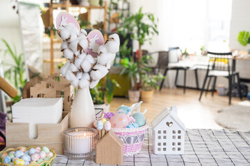 Easter decoration of colorful eggs in a basket and a rabbit on the kitchen table in a rustic style. Festive interior of a country house