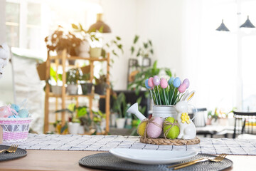 Easter decoration of colorful eggs in a basket and a rabbit on the kitchen table in a rustic style. Festive interior of a country house