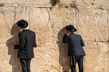 Man in kippah praying with hand on holy wall