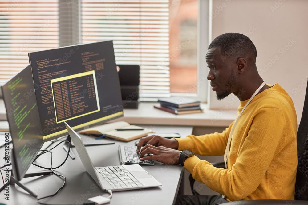 Poster side view portrait of young black man typing at keyboard and writing code in it development company