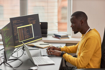 Side view portrait of young black man typing at keyboard and writing code in IT development company