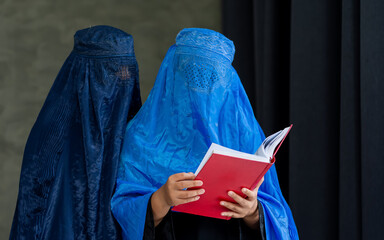 Portrait two adult beautiful Muslim women wearing headscarf, traditional dress, reading, holding...