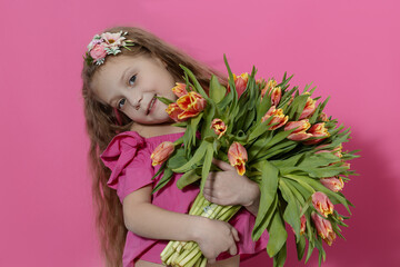 Obraz na płótnie Canvas Cute smiling child holding a beautiful bouquet of tulips in front of his face isolated on pink. Little toddler girl gives a bouquet to mom