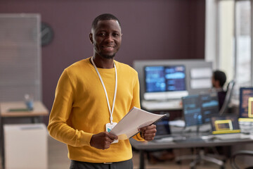 Waist up portrait of smiling black man as IT engineer standing in office, copy space