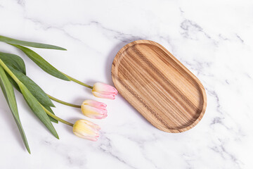 Wooden oval tray and tulips on marble background. Space for text. Top view