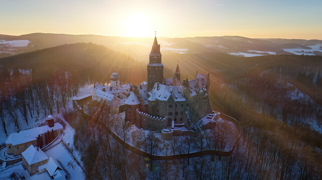 Aerial view of silhoutte of romantic, fairy tale castle in winter picturesque landscape, illuminated by the setting sun. Gothic castle, high towers, red roofs, winter highland. Bouzov castle, Moravia.