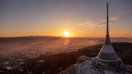 A bird's eye view of snow-covered Jested at sunrise. Photographed on the Jested ridge by drone. Beautiful winter landscape in Liberec region. - obrazy, fototapety, plakaty