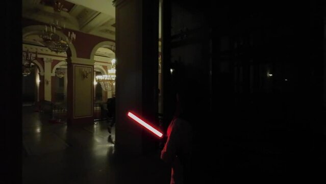 Young woman in the dark with red lightsaber have fun. Girl indoors in palace interiors, with led light lamp.