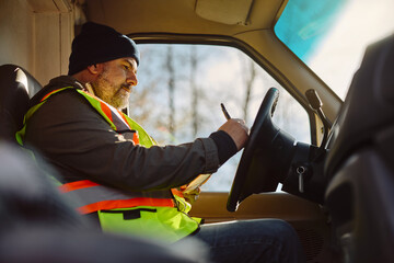 Truck driver writes on clipboard while sitting in vehicle cabin.