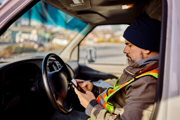 Truck driver text messaging on mobile phone in vehicle cabin.