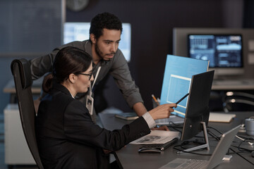 Side view portrait of two people pointing at computer screen while working in IT company