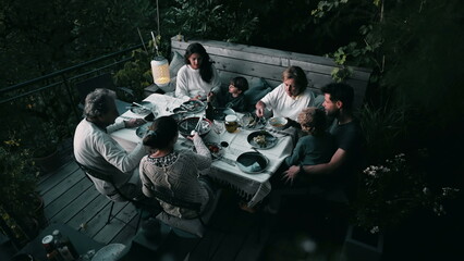 Parents and children seated at dinner table eating meal together. From above perspective of candid family enjoying food together
