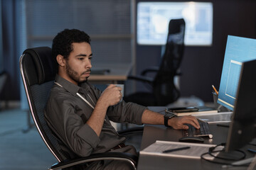 Side view portrait of man using computer and drinking coffee while working in data security office