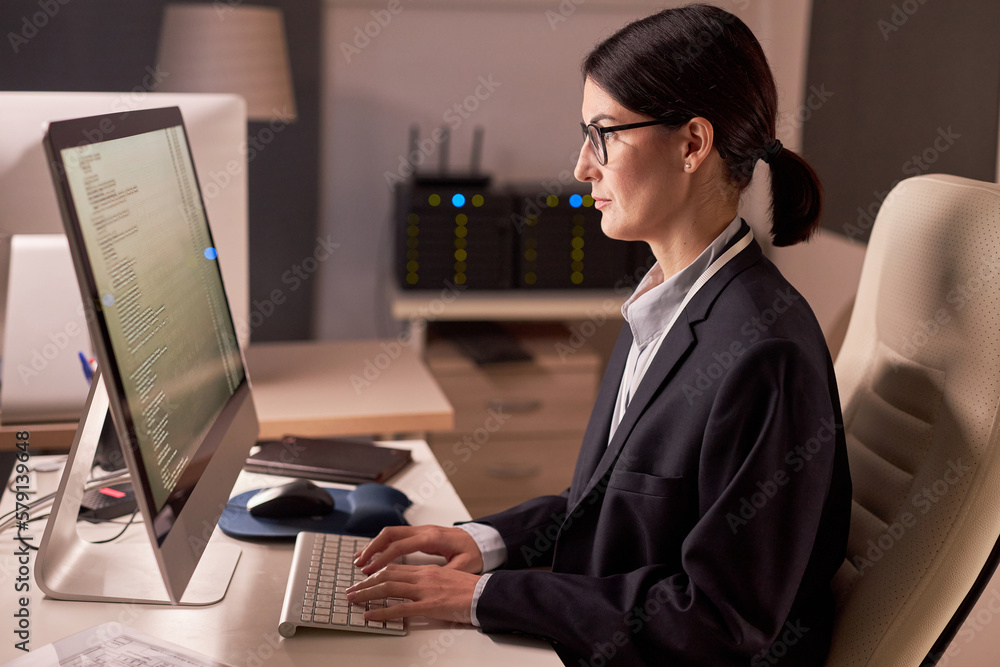 Poster side view portrait of serious businesswoman using computer while working at night in it security off